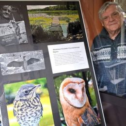 Leszek Machocki - autor zdjęć - pozuje, stojąc obok swojej wystawy