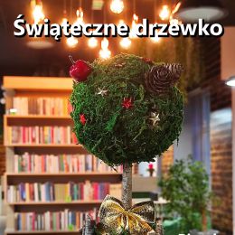 Drzewko wykonane z mchu, kory i gałęzi, udekorowane, w tle pomieszczenie biblioteki